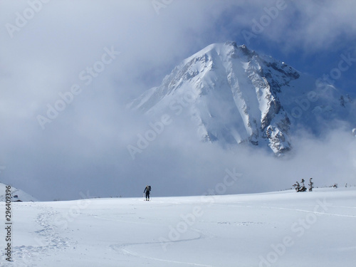 A lone backcountry skier makes his way up the Mt. Hood Cooper Spur route. Mt. Hood looms large through the clouds above the skier. He is earning his turns.