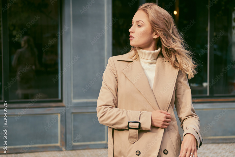 Side view of attractive girl in trench coat confidently looking away on street - obrazy, fototapety, plakaty 