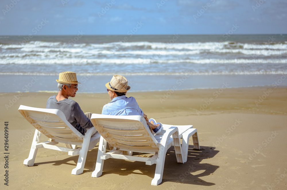 Senior couple sitting hand in hand on chairs at the beach and looking at the ocean on a good day to plan life insurance at retirement concept.