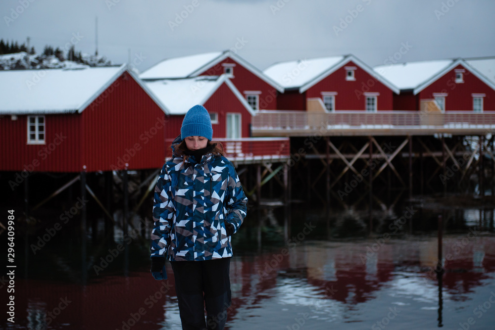 Norway. Fishing town. Girl stands by water, behind red fishing houses.