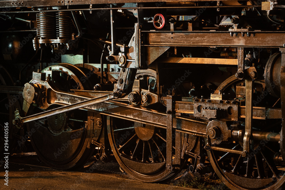 Historic steam locomotive, close up of wheels and rods at night illuminated by lights