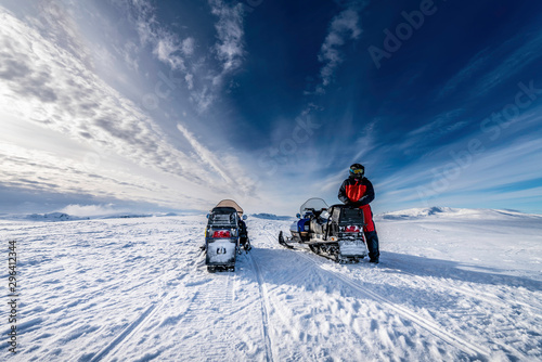 Two blue snowmobiles (back side) with a boy dressed for winter driving in cold mountains, he waits for his friend to continue the holiday adventure. Hemavan -Tarnaby area in Lappland, Sweden