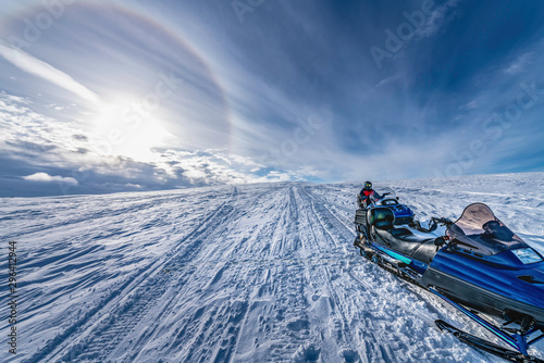 Two snowmobiles stand behind each other with a boy at second one. He dressed for driving in cold mountains, rests after long whole day ride snow desert. Hemavan, Tarnaby in Lappland, Sweden