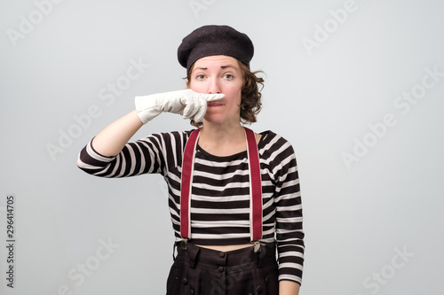 What a smell. Young unhappy mime girl squeezing nose with fingers, looking in camera with disgust expression. Studio shot