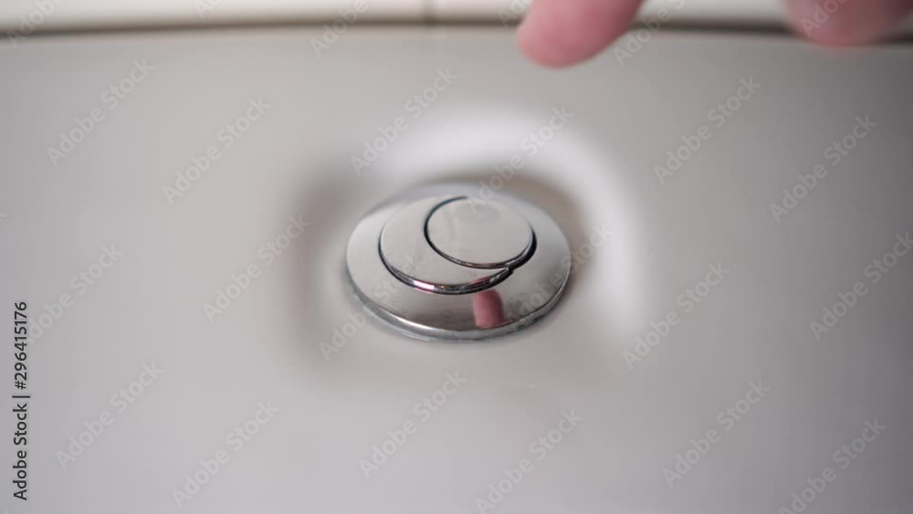 Male hand presses a shiny button of a white ceramic toilet bowl to test the performance of plumbing equipment Male hand presses a shiny button of a white ceramic toilet bowl to test the performance of plumbing equipment