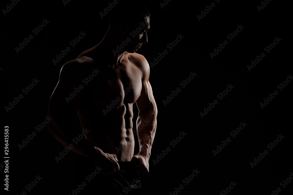 Muscular model sports young man in jeans showing his press on a black background. Fashion portrait of sporty healthy strong muscle guy. Sexy torso. - obrazy, fototapety, plakaty 