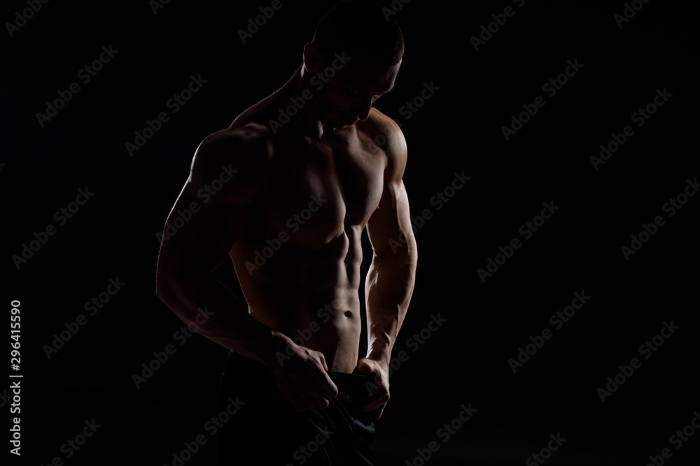 Muscular model sports young man in jeans showing his press on a black background. Fashion portrait of sporty healthy strong muscle guy. Sexy torso.