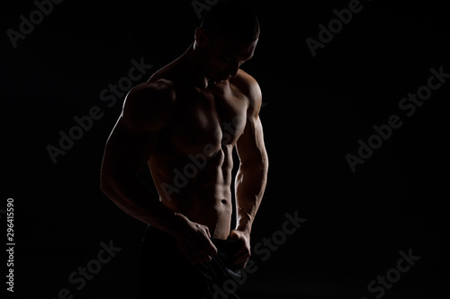 Muscular model sports young man in jeans showing his press on a black background. Fashion portrait of sporty healthy strong muscle guy. Sexy torso.