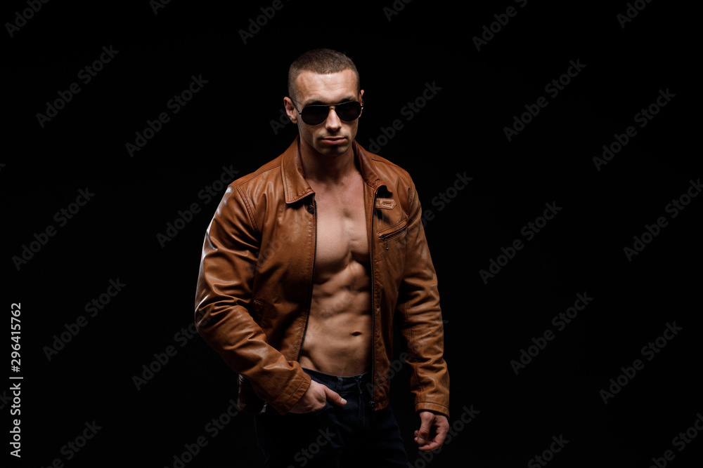 Muscular model sports young man in jeans showing his press on a black background. Fashion portrait of sporty healthy strong muscle guy. Sexy torso.