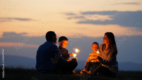 Parents and children silhouettes holding fireworks  sunset sky  celebration