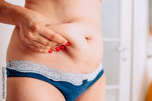 Overweight woman hand holding or pinching fat body belly paunch in bathroom.