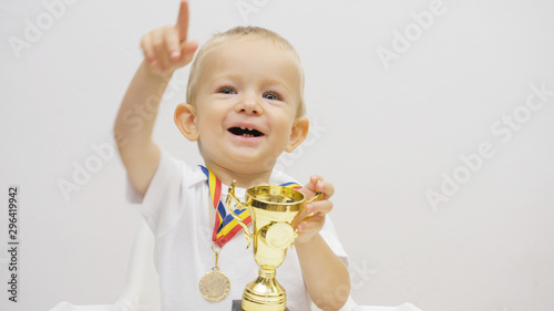 Blond hair baby child wit medal hold champion cup thankful point  finger up photo