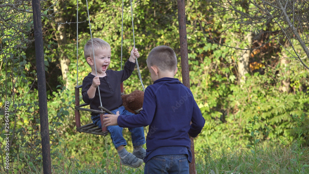 Baby child on swing playing with his brother, have fun in green garden together Baby child on swing playing with his brother, have fun in green garden together