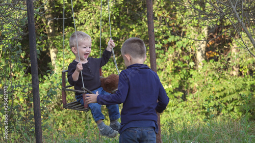 Baby child on swing playing with his brother,  have fun in green garden together