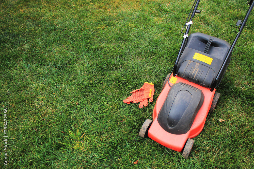 An electric lawn mower with a grass box and gloves is on the grass. An electric lawn mower with a grass box and gloves is on the grass.