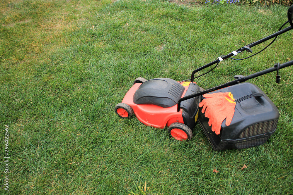 An electric lawn mower with a grass box and gloves is on the grass. An electric lawn mower with a grass box and gloves is on the grass.