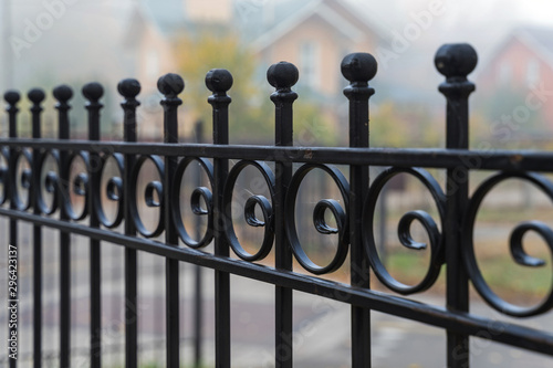 Beautiful metal fence on the background of houses in the fog in the autumn. Guardrail close up.