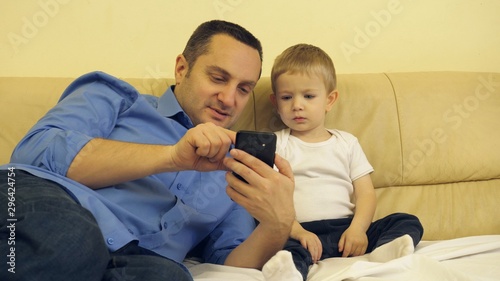 Father and little sit on coach son looking at phone, lazy Sunday