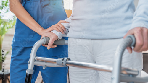 Cropped image of nurse helping senior woman to walk with walker at home photo
