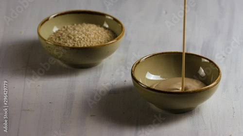 Tahini, sesame paste with sesame seeds on a wood background.