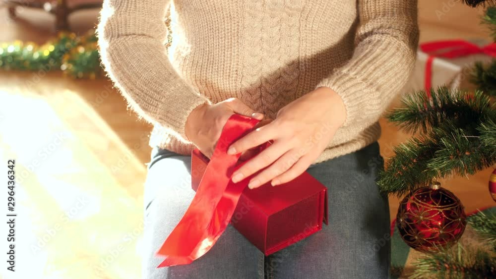 4k video of young woman tying red ribbon bow on box with Christmas present