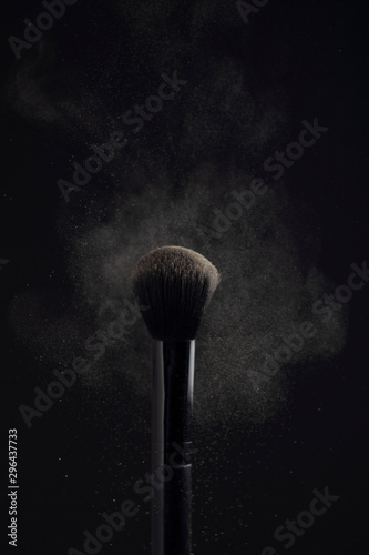 powderbrush with cloud of face powder on black background photo