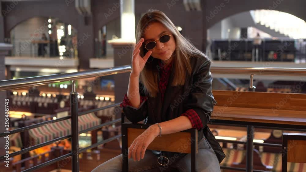A beautiful modern young European girl with white hair in a black leather jacket and jeans sits indoor cafe on an autumn beautiful day. Positive emotions. Modern woman. Fashionable clothes A beautiful modern young European girl with white hair in a black leather jacket and jeans sits indoor cafe on an autumn beautiful day. Positive emotions. Modern woman. Fashionable clothes