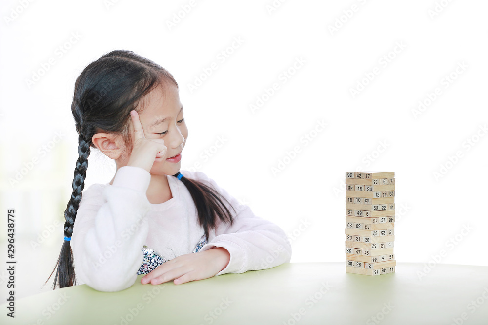 Intend little Asian child girl thinking to playing wood blocks tower game for Brain and Physical development skill in a classroom. Focus at children face. Kid learning and mental skills concept. Intend little Asian child girl thinking to playing wood blocks tower game for Brain and Physical development skill in a classroom. Focus at children face. Kid learning and mental skills concept.