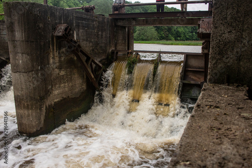 The dam on the river. Water intake facility to limit the flow of water. The old dam. A river with a small riverbed. Metal concrete construction.