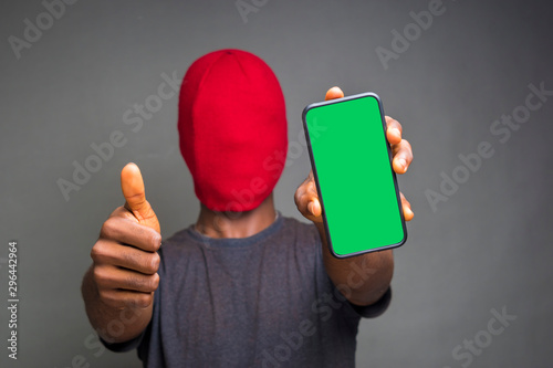 young african hacker holding  at a green screen phone and did thumbs up photo