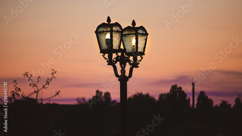 Vintage old lit lightpost at the dusk. Sunset sky on the background