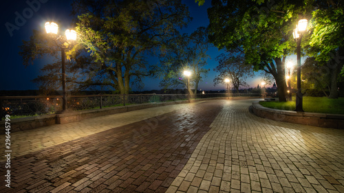Empty city park landscape at the late evening or night with lit lightposts and brick road