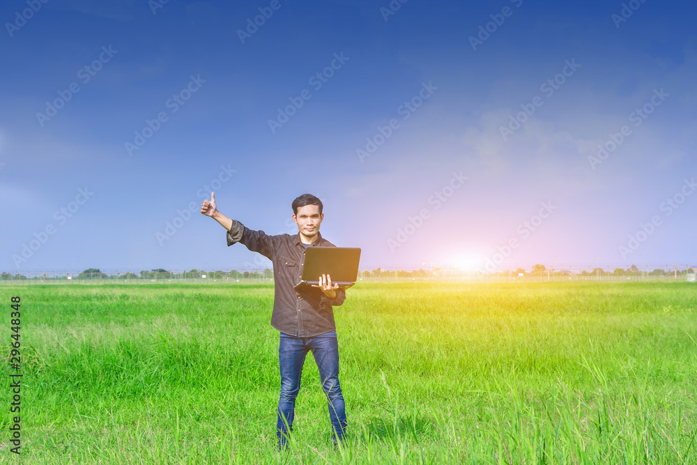 Man holding computer on green field at sunset under blue sky,Design background texture and concept Man holding computer on green field at sunset under blue sky,Design background texture and concept