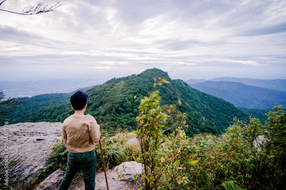 Naklejka premium Trekker sitting on the mountain with Beautiful Sunrise and sea of mist in the morning on Khao Luang mountain in Ramkhamhaeng National Park,Sukhothai province Thailand