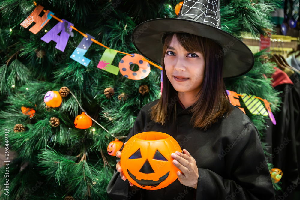 Fototapeta premium Beautiful young surprised woman or Halloween Witch dark style with holding a pumpkin in Halloween celebrate night party. Copy space background and soft or select focus