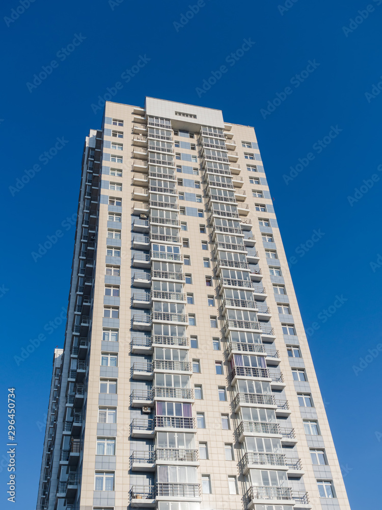 A new high-rise residential building rises in the clear sky. Bottom view. Light tall and narrow facade on a blue sky background