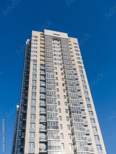 A new high-rise residential building rises in the clear sky. Bottom view. Light tall and narrow facade on a blue sky background