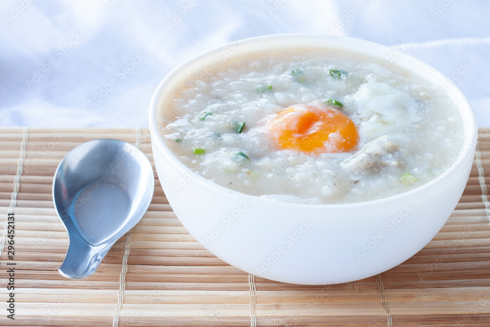 Rice porridge or congee with egg in white bowl and spoon on wooden table. Rice porridge or congee with egg in white bowl and spoon on wooden table.