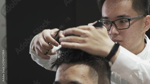 Close-up Asian hairdresser with glasses combing and cutting hair to client in salon. Creates a modern hairstyle