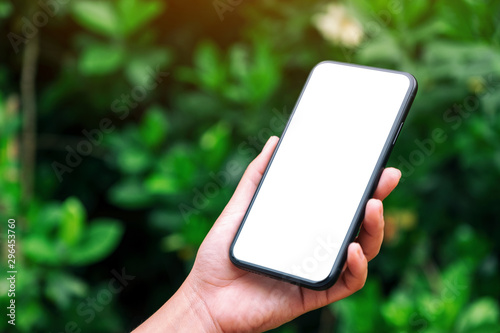 Mockup image of hands holding black mobile phone with blank desktop screen with green nature background photo