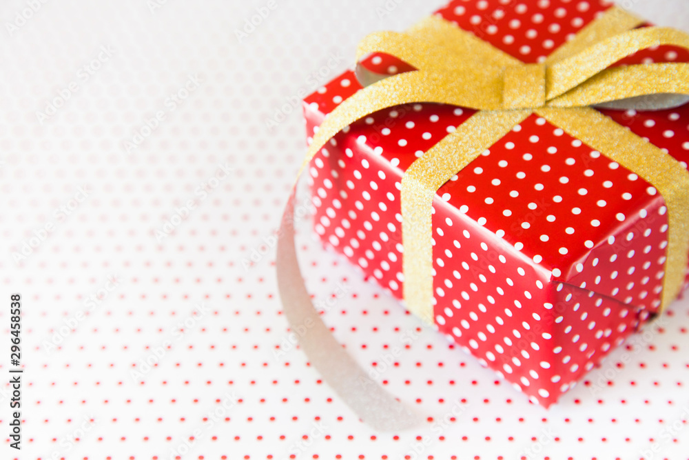 Red gift with gold ribbon on the white polka dot background