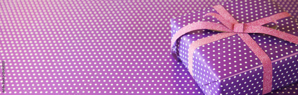 Obraz premium Violet gift with pink ribbon on the violet polka dot background