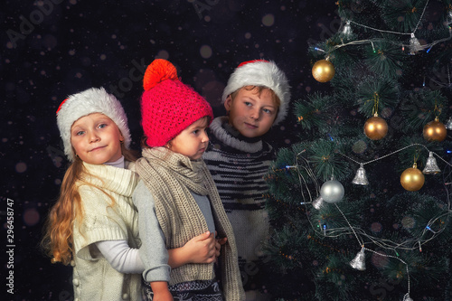 Children at the Christmas tree . Little girls in warm sweaters and knitted hats on Christmas eve