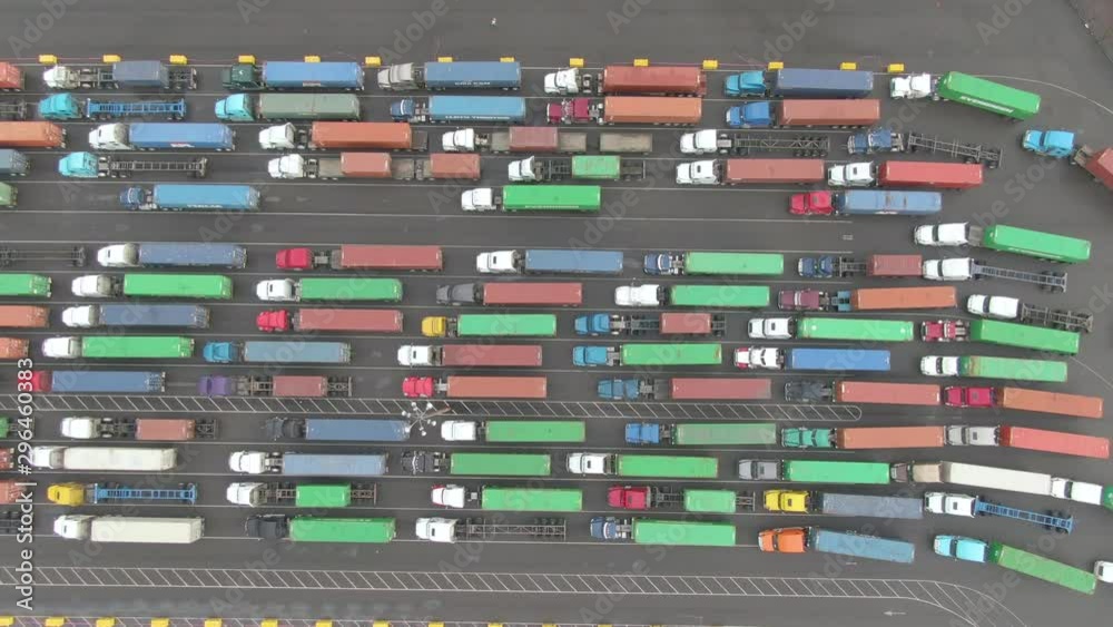 DRONE, TOP DOWN: Flying above a small group of trucks driving between others waiting in the Port of LA. Couple of trucks get to drive past the long line waiting to be dispatched from the busy harbor.