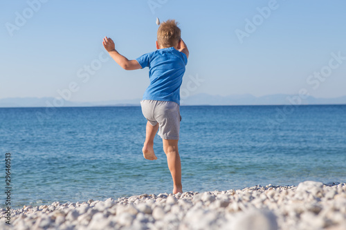 funny little boy jumping high on beach near sea shore in summer