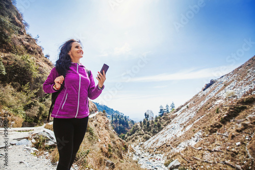 Sticker Beautiful sporty woman using her phone while trekking outdoors in Dharamsala, In