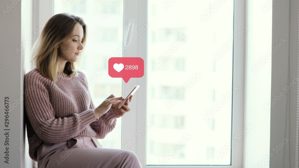 Woman blogger browsing phone sitting on window, infographic sign with numbers and growing likes counter over smartphone. Concept of modern work and popularity in social media. Woman blogger browsing phone sitting on window, infographic sign with numbers and growing likes counter over smartphone. Concept of modern work and popularity in social media.