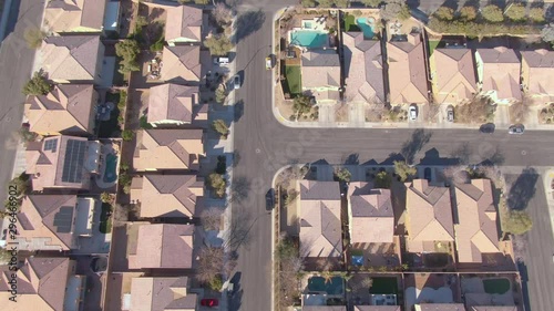AERIAL TOP DOWN: Flying over terraced houses in a luxury suburban neighborhood in Nevada. Cinematic shot of row houses and backyards in the sunny suburbs of Las Vegas. Empty roads run through suburbia