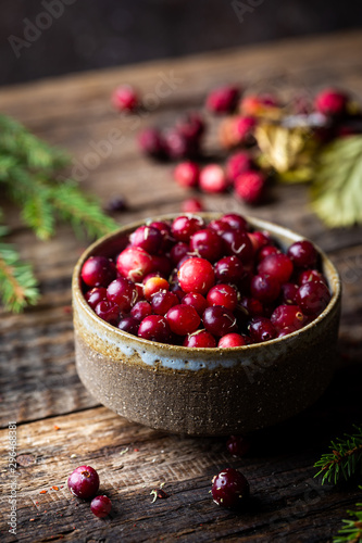 Cranberries in a handmade bowl on rustic wooden background.