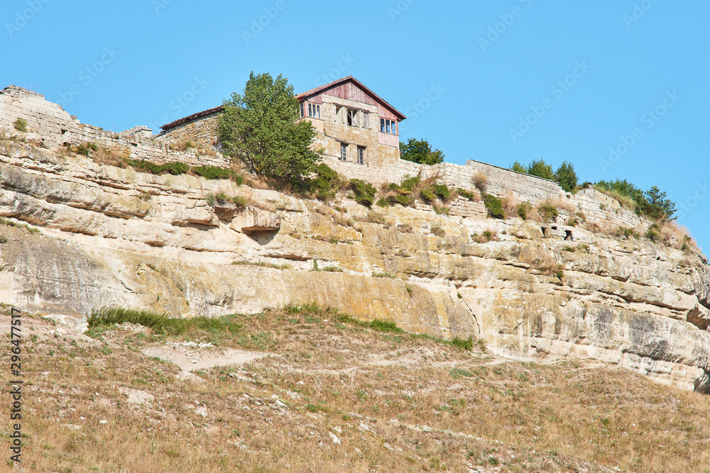 Ancient abandoned building on a cliff top. Stone house over a cliff. Sunny summer day, clear blue sky.